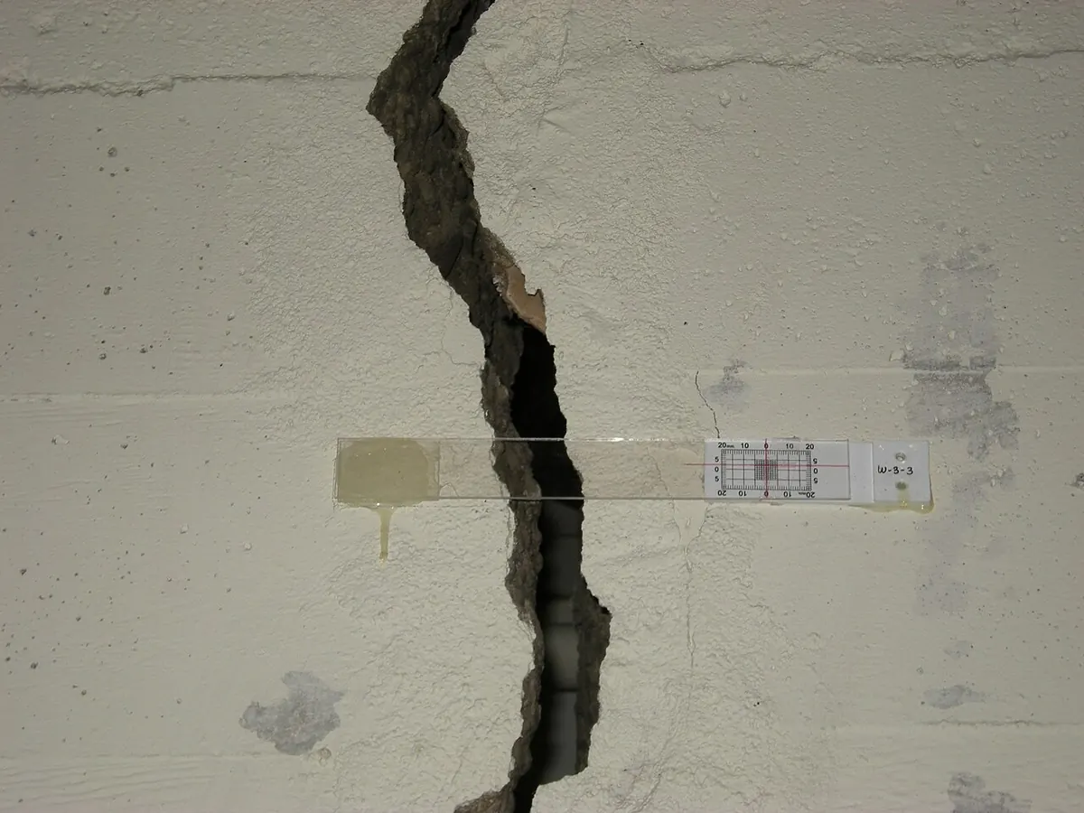Wide crack in an interior wall with a crack gauge